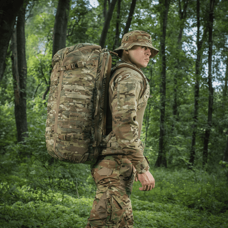 M-Tac Rygsæk Gen.II Elite Large, henkilö metsässä camokuvioisen repun kanssa; kestävä reppu ulkoiluseikkailuihin.
