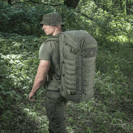 M-Tac Rygsæk Gen.II Elite Large, mies kantaa reppua metsässä; reppu valmistettu kestävästä Cordura-materiaalista, sopii ulkoiluseikkailuihin.