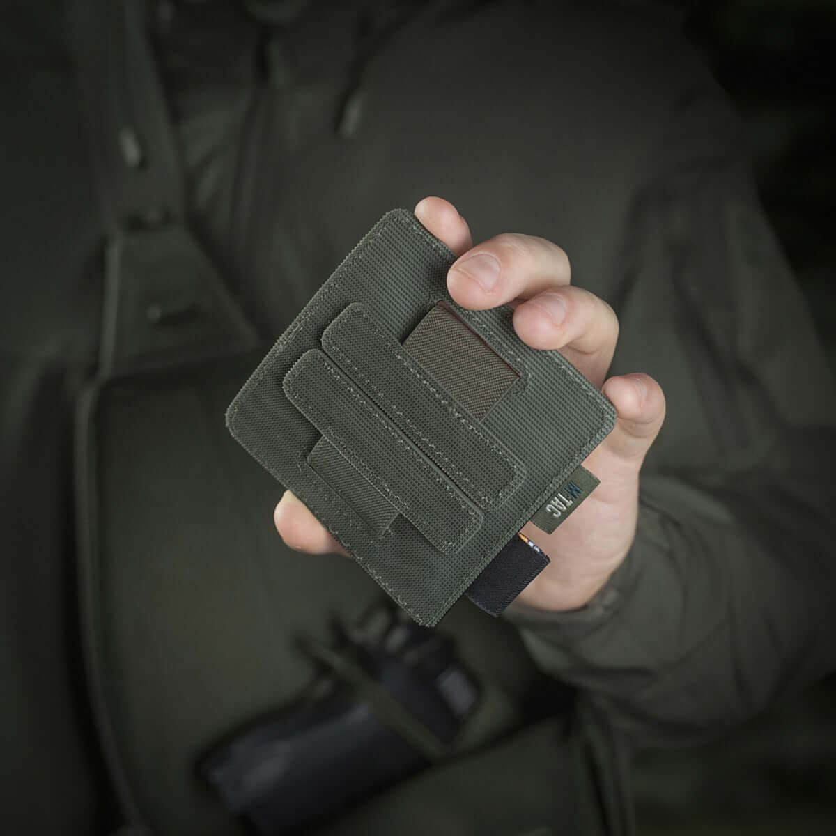 Henkilö pitelee M-Tac Double Mag Pouch Hook Backed Magazinea, sopii pistoolin lipuille ja multitoolille, kiinnitetty Velcrolla