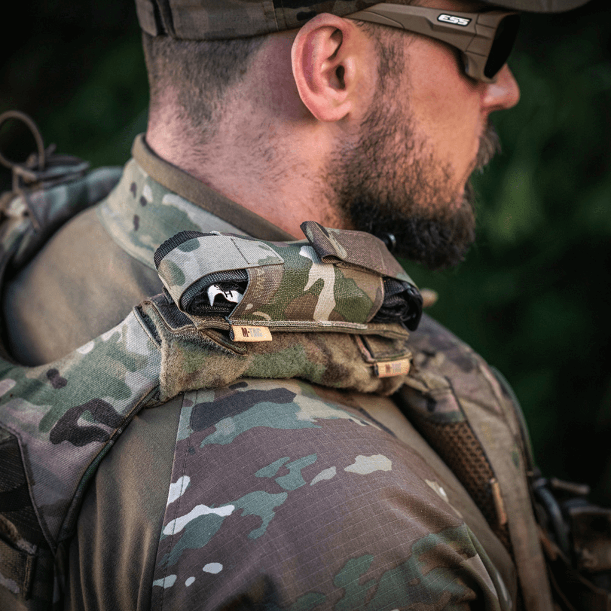 M-Tac Tourniquet Pouch Elastisk med MOLLE Gen.II taktiikkapukuisen miehen olkapäällä ulkona, nopea pääsy.