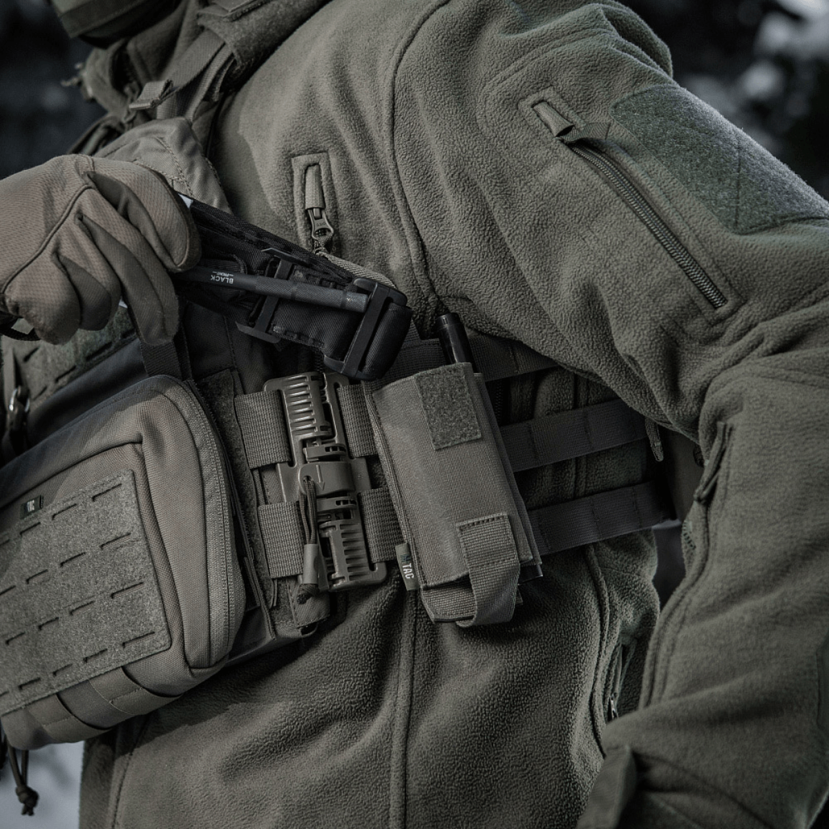 M-Tac Elastinen turnikekotelo Molle Gen.III kiinnitetty taktiseen liiviin, osoittaa nopeaa käyttöä ja turvallista säilytystä tourniquetille.