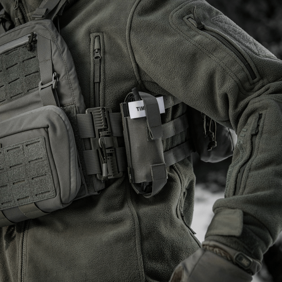 M-Tac Elastinen turnikekotelo Molle Gen.III kiinnitetty taktiseen takkiin henkilöllä kentällä.