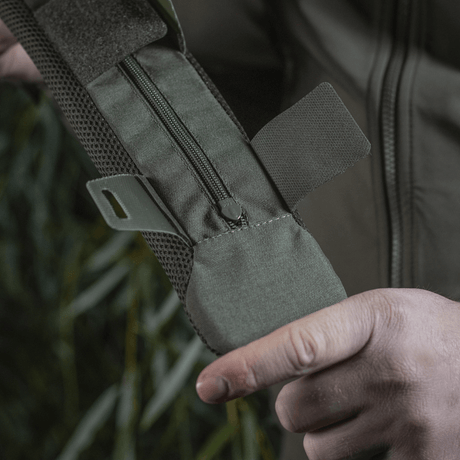 Henkilö pitelee M‑Tac olkahihnan pehmikettä 50 mm Elite robustista Cordura-materiaalista, vetoketjukiinnitys ja 3D-mesh-ventilaatio.