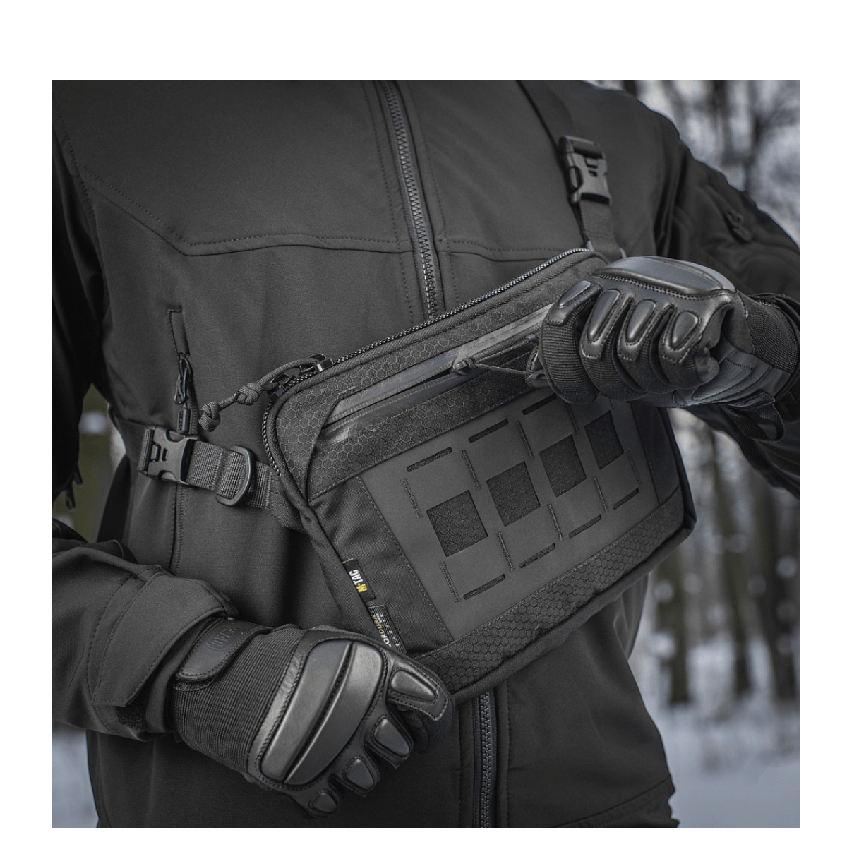Henkilö mustassa takissa esittelee M-Tac Admin-laukku Eliteä, valmistettu kestävästä Cordura-materiaalista, vetoketjuilla ja korkealaatuisilla soljilla