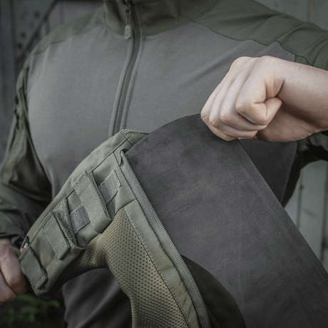 Henkilö näyttää M-Tac olkatyynyn kiinnityksen takkiin Velcro-kiinnitysjärjestelmällä
