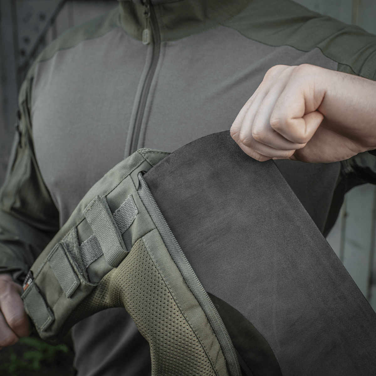 Henkilö näyttää M-Tac olkatyynyn kiinnityksen takkiin Velcro-kiinnitysjärjestelmällä