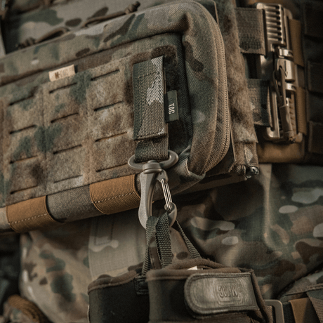M-Tac karabiinihaka-lisävaruste kiinnitetty taktiseen MOLLE-reppuun, helppo avata ja säädettävä Velcro-remmi.