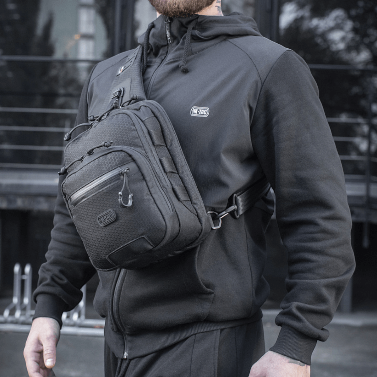Henkilö kantaa M-Tac Cross Taske Slim Elite Hex -laukkua, pukeutunut mustiin, ulkona.
