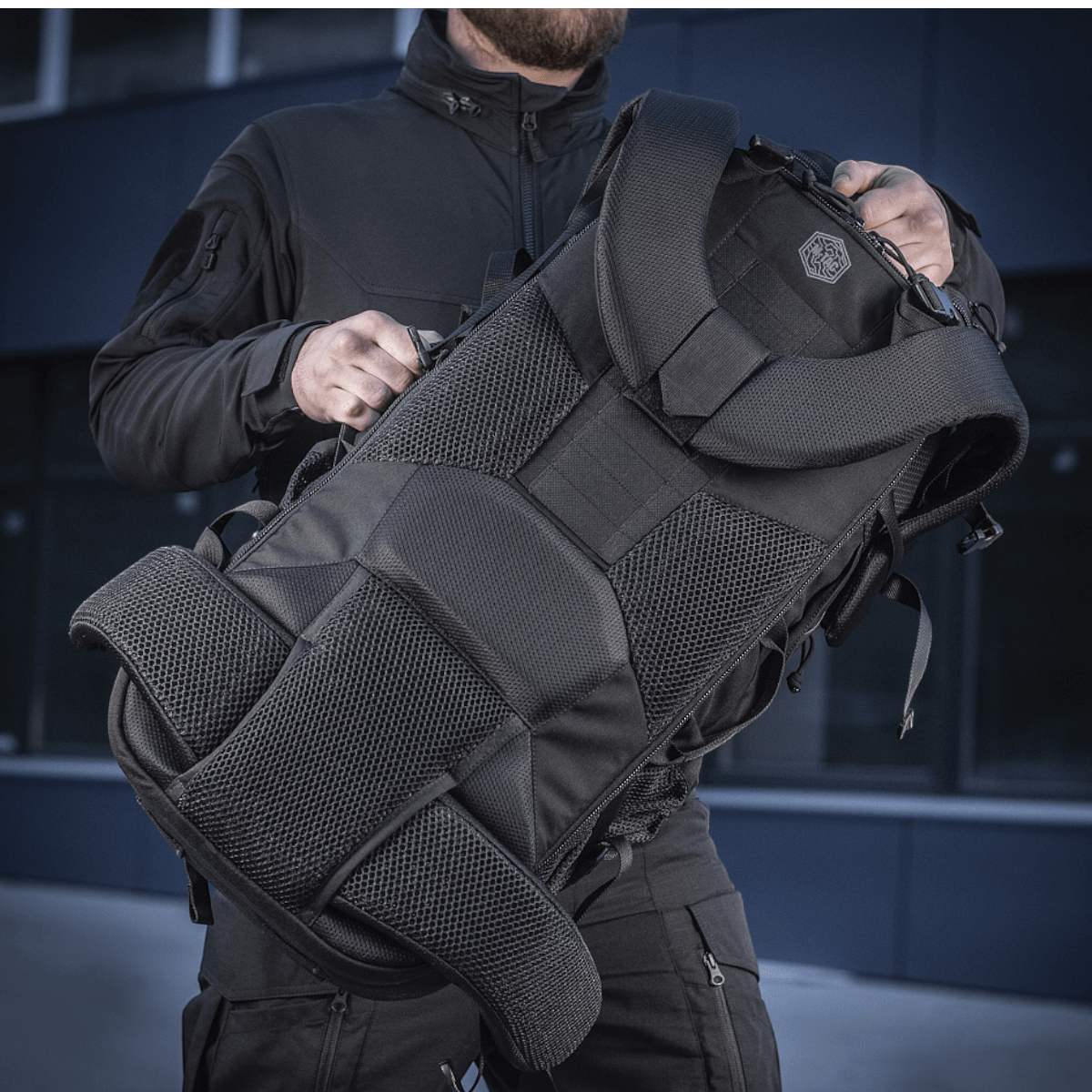 Henkilö pitää M-Tac Rygsæk Large Elite Hex Gen. IV -reppua ergonomisella muotoilulla ja kestävillä materiaaleilla, sopiva aseiden kuljetukseen.