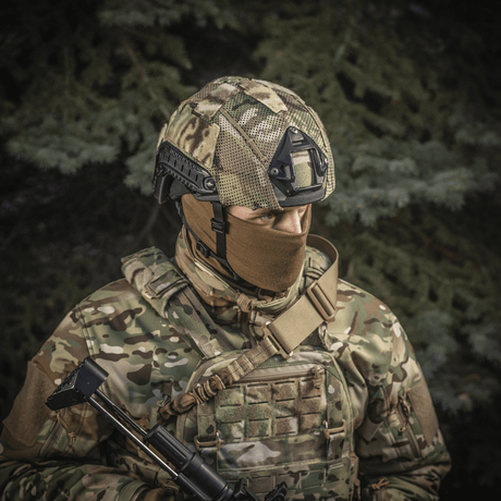 Sotilas pukeutuneena M‑Tac Hjelmcover Shroud Elite MULTICAM-maastokuviossa, suunniteltu TOR-D-kypärille tehokkaaseen naamiointiin maastossa.