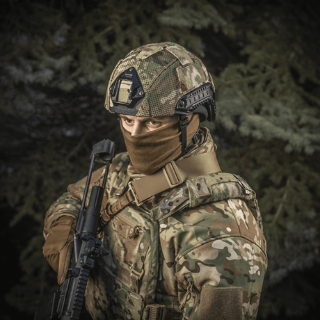 Sotilas pukeutuneena M‑Tac Hjelmcover Shroud Elite MULTICAMissa TOR-D-kypärälle, ase mukanaan metsämaisemassa.
