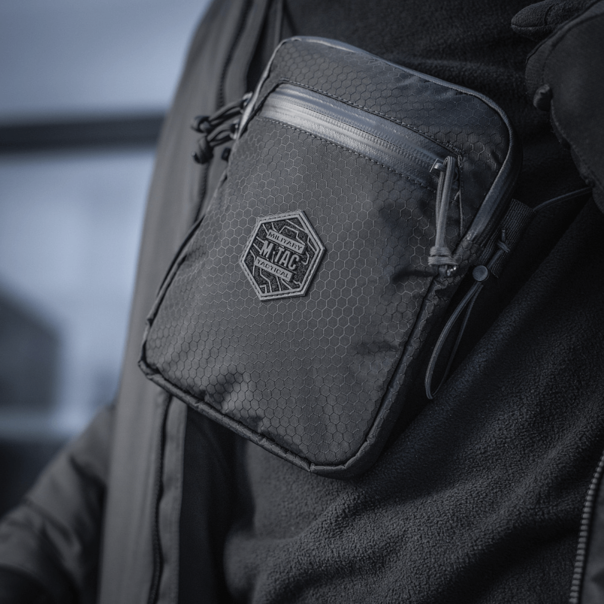 Henkilö kantaa pientä, vankkaa M‑Tac Pocket Bag Elite HEX:ää kulutusta kestävin YKK-vetoketjuin, sopii arjen säilytystarpeisiin.