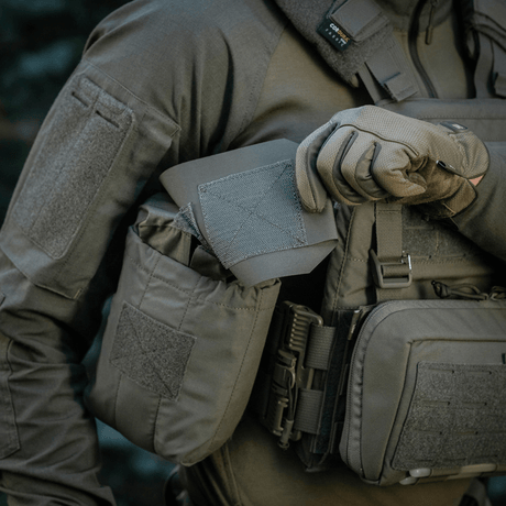 Henkilö taktiseen asuun pukeutuneena pitää M‑Tac Medic Pouch Vertical Large Eliteä, innovatiivinen lääkintälaukku valmistettu kestävästä Cordura 500D -materiaalista.
