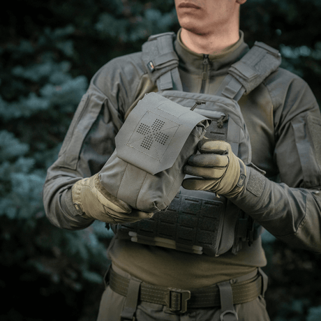 Henkilö pitää M‑Tac Medic Pouch Vertical Large Eliteä kestävästä Cordurasta, ihanteellinen ensiapuvälineille ja nopeaan pääsyyn.