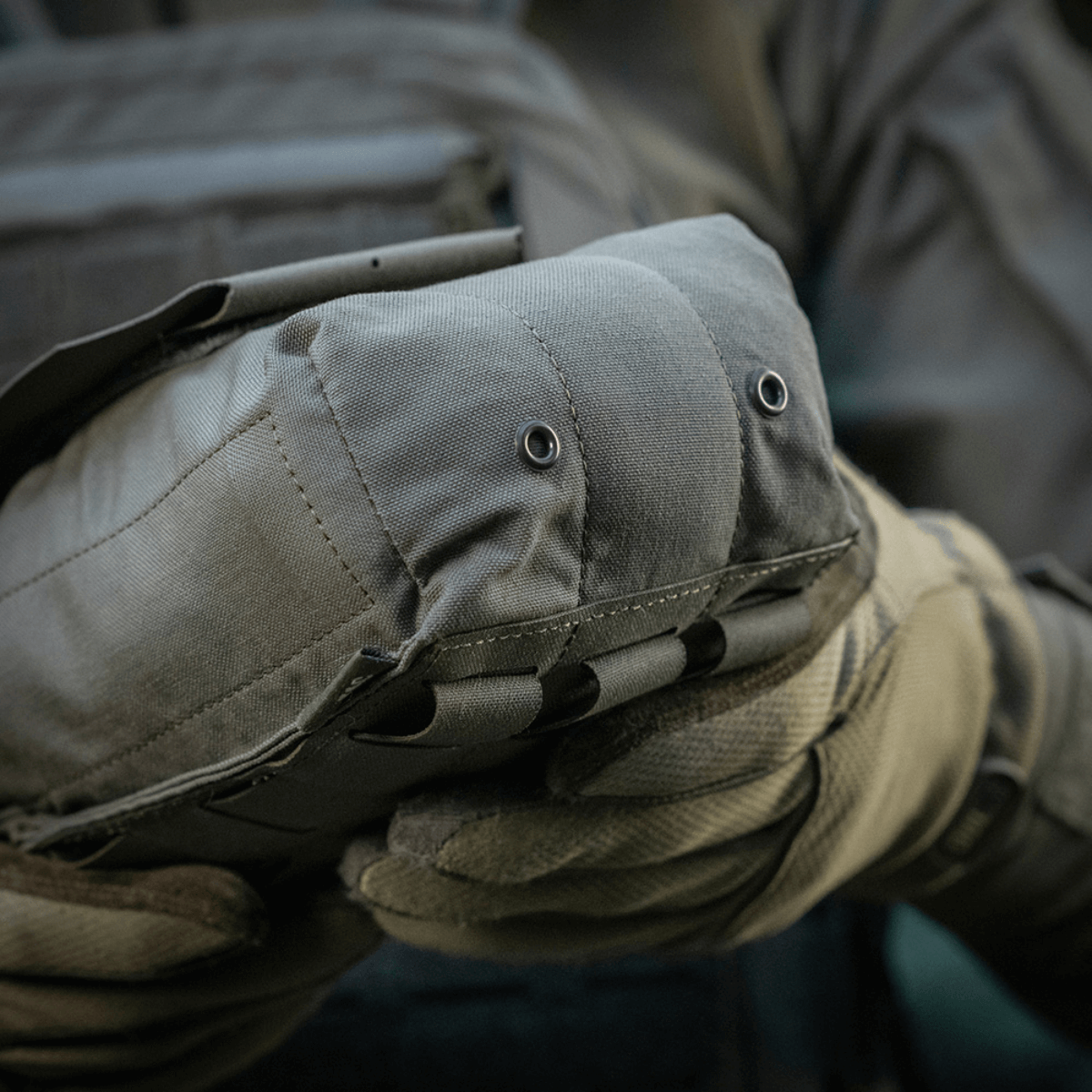 M‑Tac Medic Pouch Vertical Large Elite kestävässä Cordura 500D:ssä, lääkinnällisten välineiden turvallinen säilytys, pidettynä hansikkaisiin pukeutuneen henkilön toimesta.