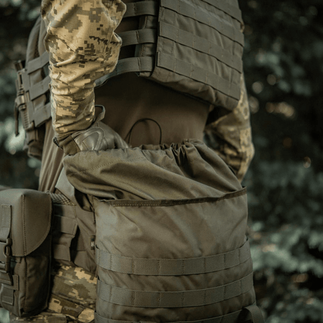 Henkilö kantaa M-Tac Pouch Sukharka Gen.3 XL:ää kiinnitettynä MOLLE-järjestelmään; näyttää Cordura 500D -materiaalin kestävyyden kentällä.