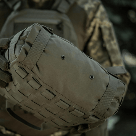 M-Tac Pouch Sukharka Gen.3 XL sotilaan pitelemänä metsäympäristössä; Cordura 500D, MOLLE-järjestelmä ja Velcro-paneli.