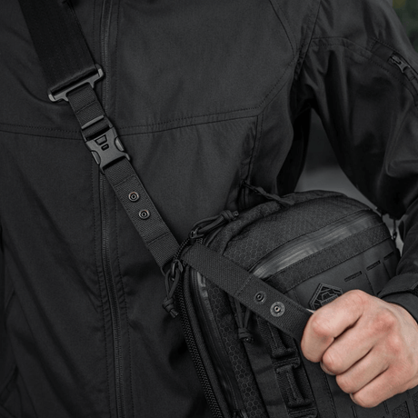 M-Tac Tablet Bag Laser Cut Hex henkilön kantamana, näyttää Cordura-materiaalin ja Laser Cut MOLLE -muotoilun; sopii EDC:lle, asiakirjoille ja tabletille.