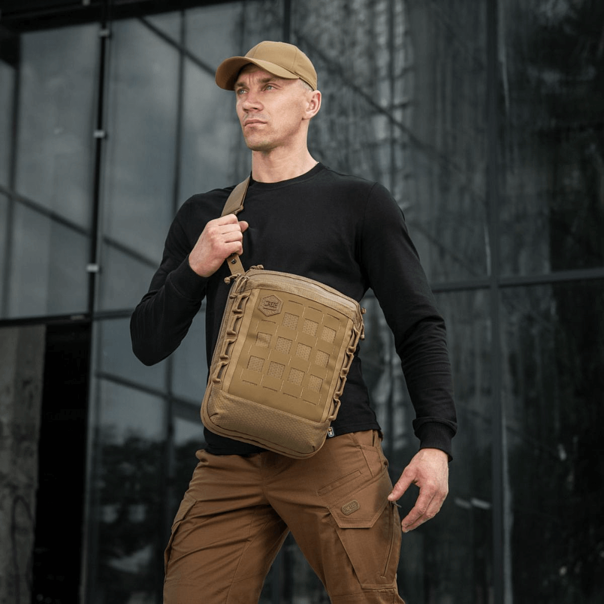 Mies kantaa M-Tac Tablet Bag Laser Cut Hex edessä toimistorakennusta, huomaamaton olkalaukku EDC:lle ja asiakirjoille.