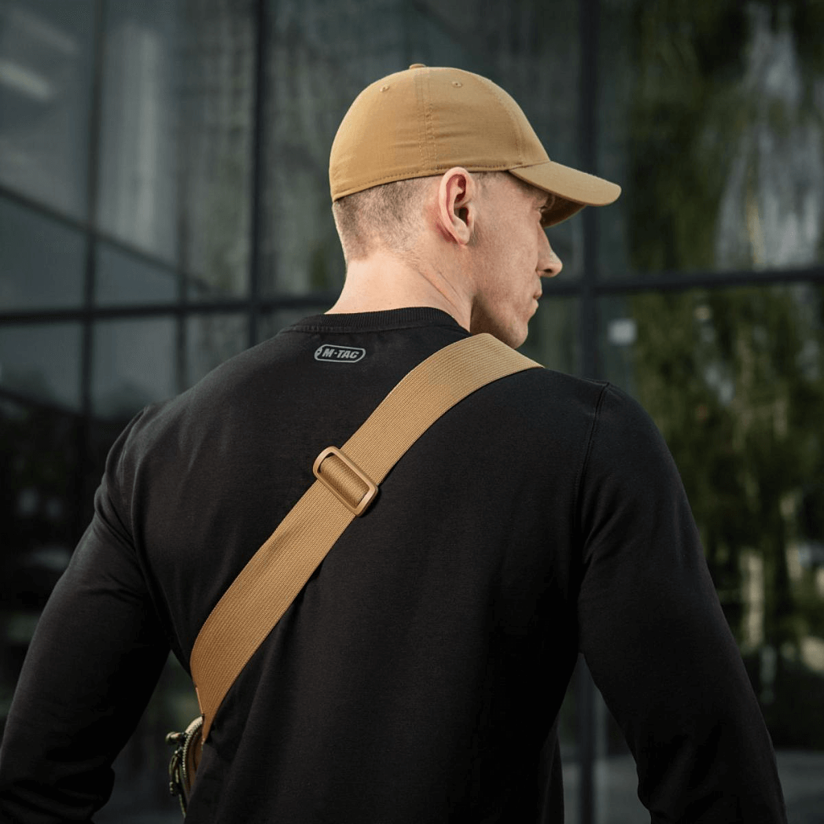 Mies mustassa paidassa ja beigessä lippiksessä nähtynä takaa, M-Tac Tablet Bag Laser Cut Hex vinosti olkapäällä.