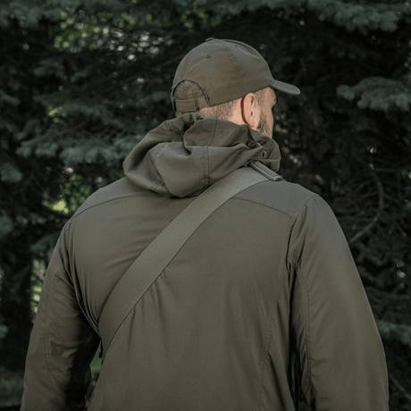 Mies metsässä M-Tac Tablet Bag Laser Cut Hex olkapäällä, päällään armeijanvihreä takki ja lippalakki.
