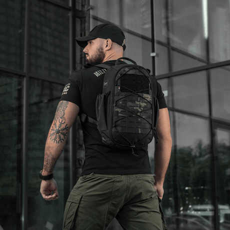 Mies kantaa M-Tac STURM Elite -reppua 15 l, musta väri, suunniteltu lyhytaikaisiin kenttäoloihin, MOLLE Laser Cut -paneelilla.
