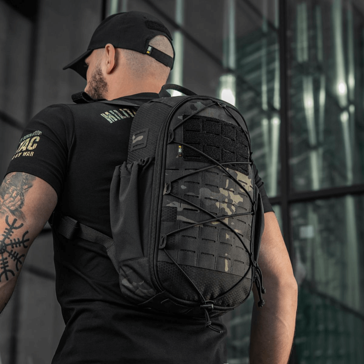 Mies kantaa M-Tac STURM Elite -reppua MOLLE Laser Cut -etupaneelilla urbaanissa ympäristössä, taktinen ja kestävä, suunniteltu lyhytaikaisiin kenttäretkiin.