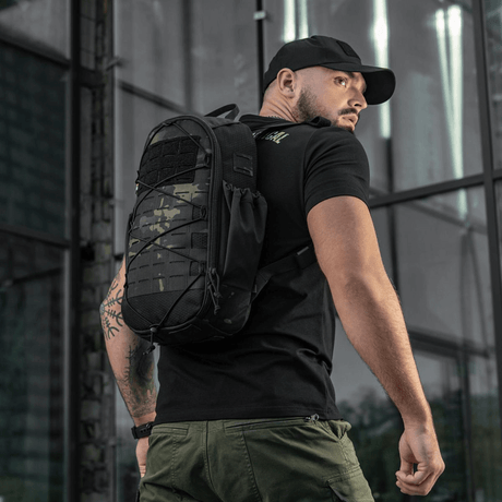 Mies kantaa M-Tac STURM Elite -reppua MOLLE Laser Cut -etupaneelilla ulkoilmassa.