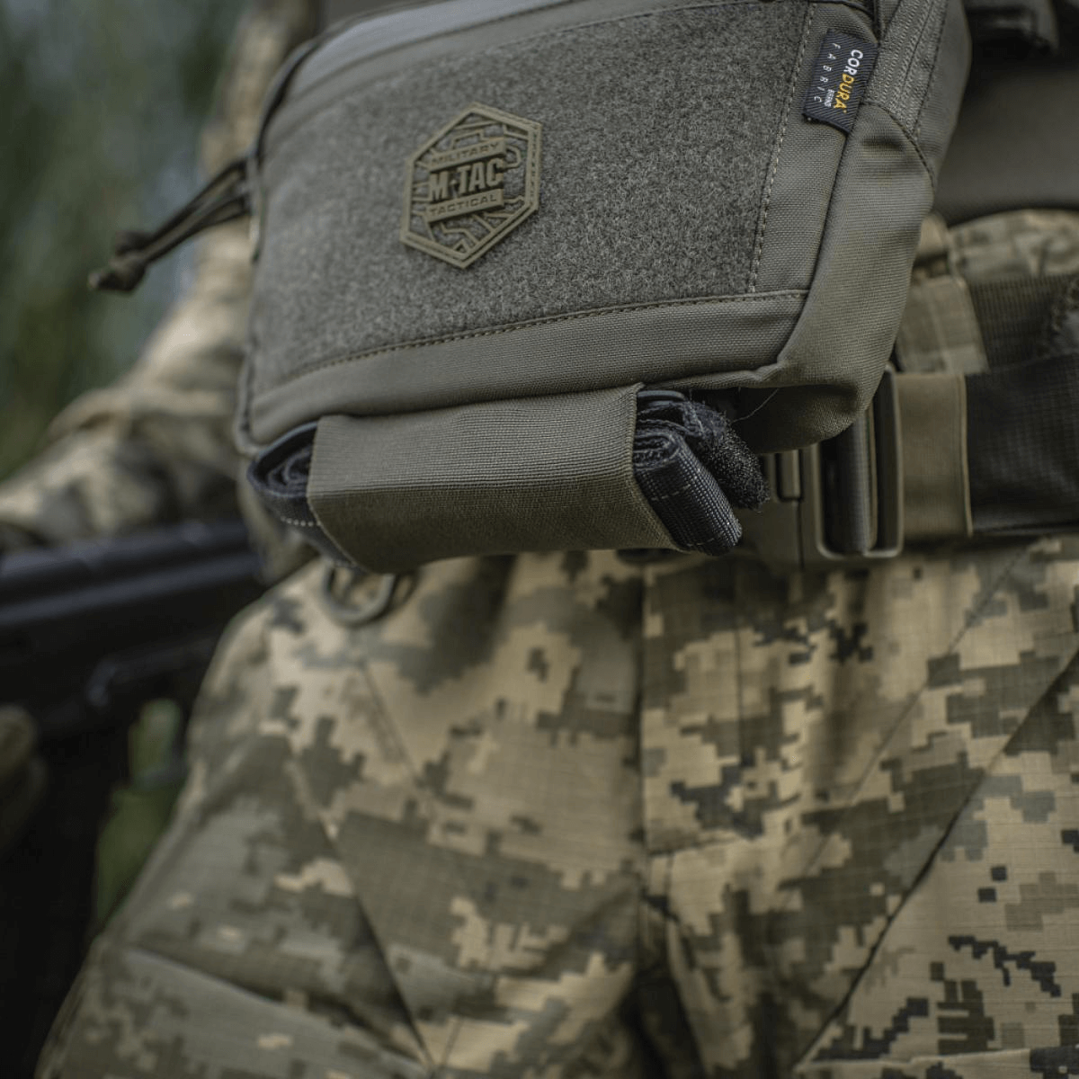 M-Tac Large Elite Gen.II olkalaukku, taktinen olkalaukku Cordura 500D:stä YKK-vetoketjuilla, nähtynä maastokuvioidun univormun päällä.
