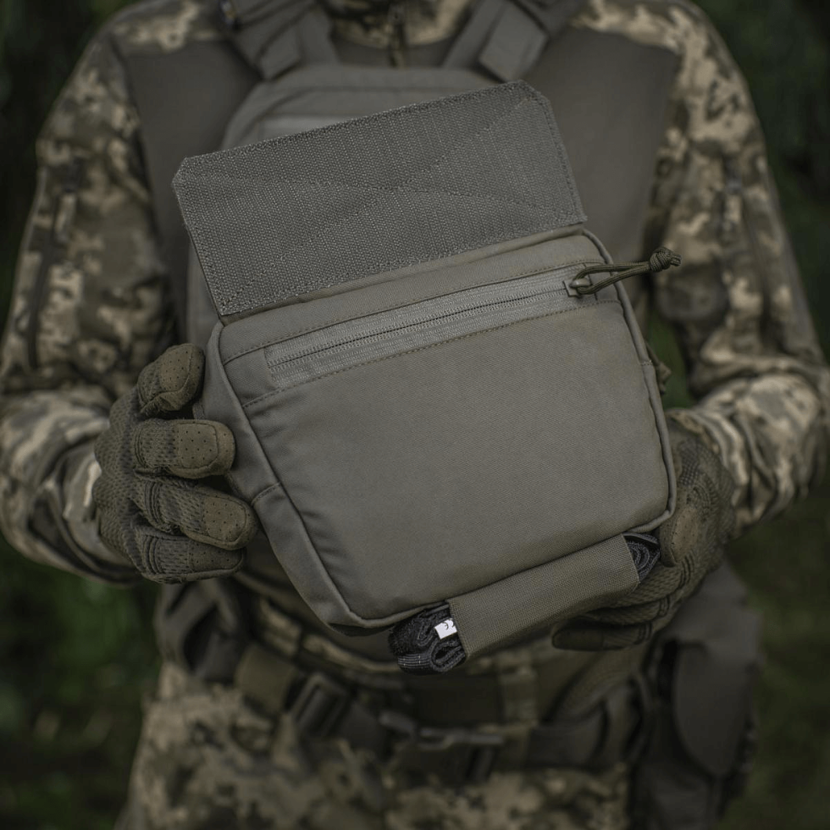 M-Tac Large Elite Gen.II olkalaukku maastokuvioidussa asussa olevan henkilön kädessä, valmistettu Cordura 500D:stä, YKK-vetoketjut.