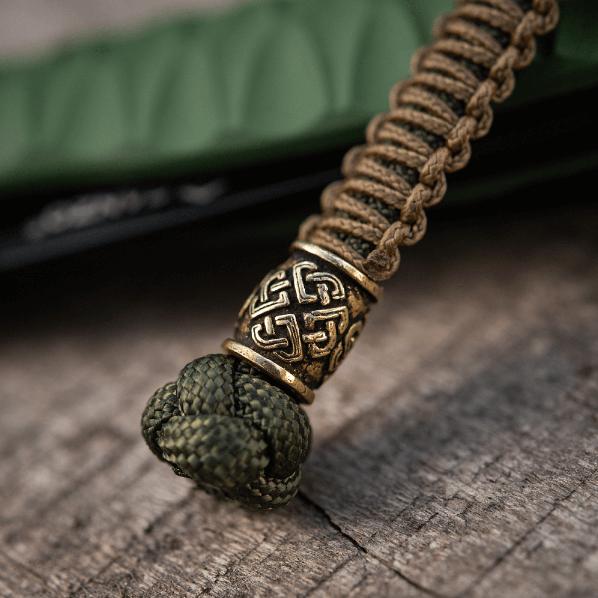 M-Tac Knife Lanyard Celtic, punottu paracord kelttikuvioinnilla, veitsilisävaruste puumaisella pinnalla.