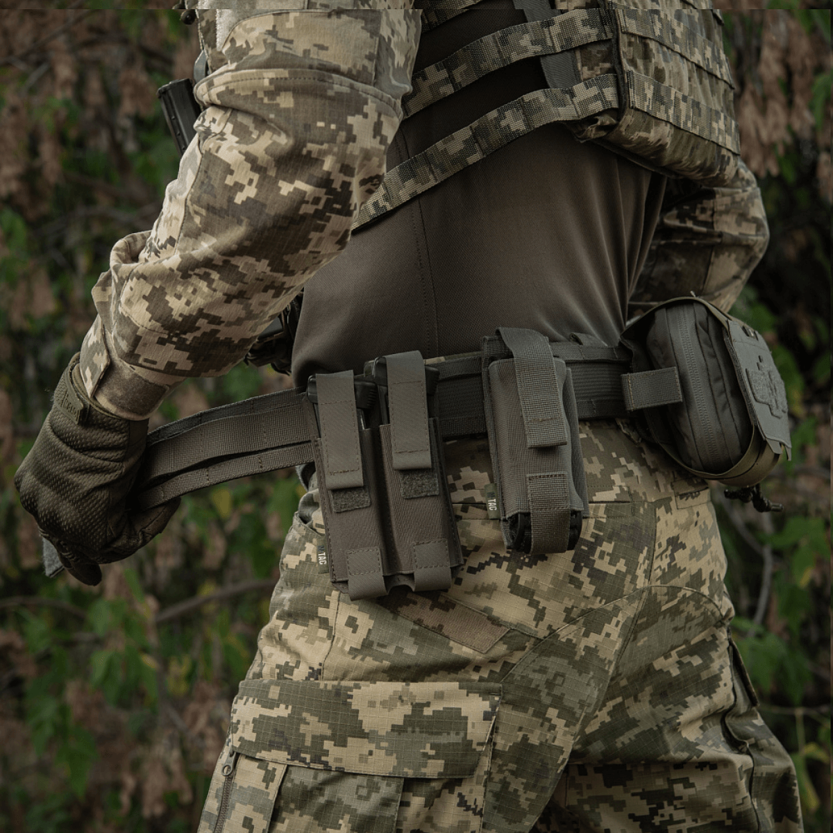 M-Tac Range -vyö Cobra Buckle Gen.IV taktisen varustuksen päällä lipastaskuilla ja ensiapuvälineillä maastokuviossa.