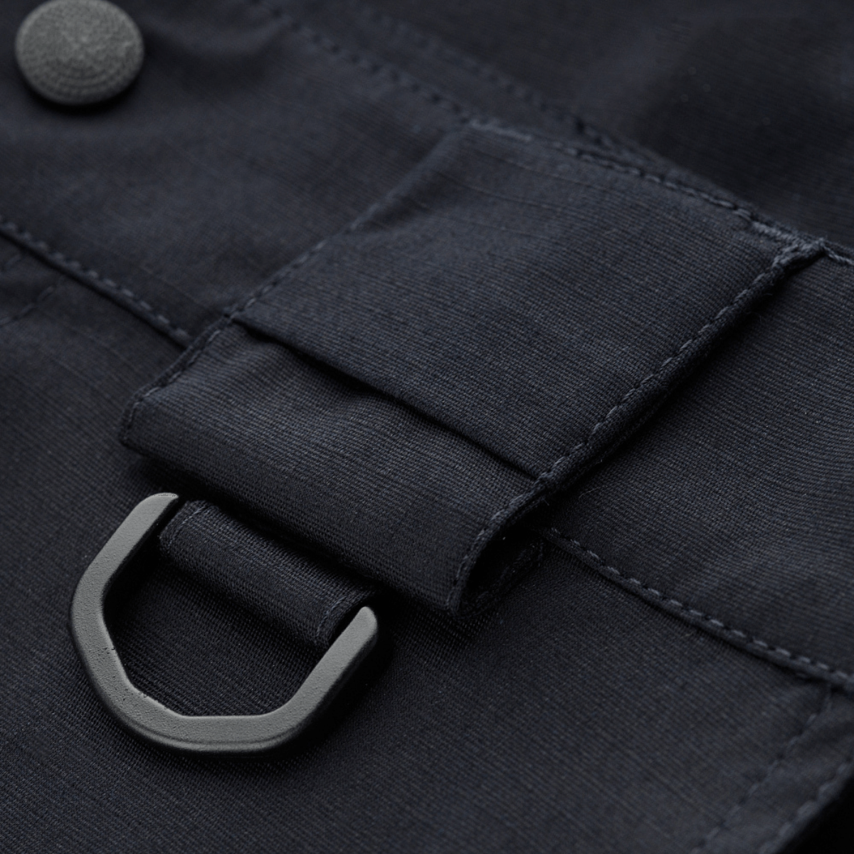 Yksityiskohta M-Tac Shorts Aggressor Gen.II Flexistä mustassa ripstop-materiaalissa, D-rengas ja nappi.
