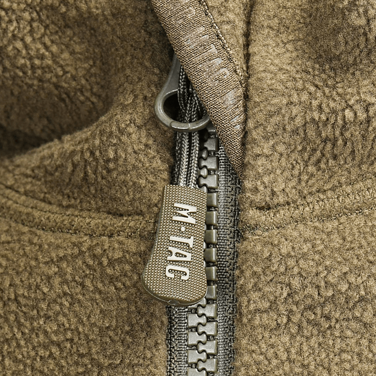 Lähikuva M-Tac Lite Microfleece Hættetrøje -vetoketjun vetimistä ruskeassa fleecessä M-Tac-logolla.