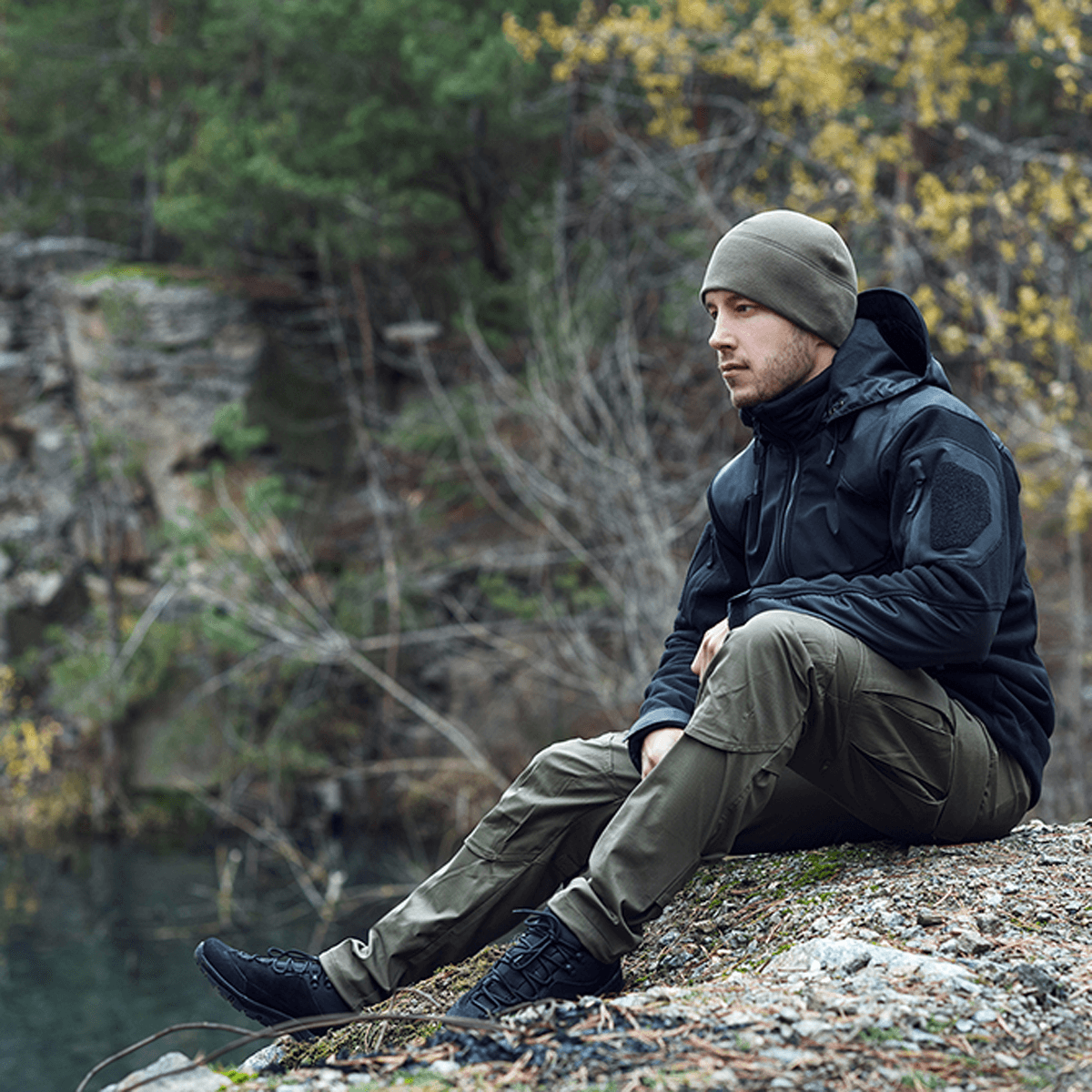 Mies pukeutuneena M-Tac Norman Windblock -fleecetakkiin istuu ulkona metsässä, sopii viileään säähän. Lämmin ja tuulenpitävä softshell-paneeleilla.