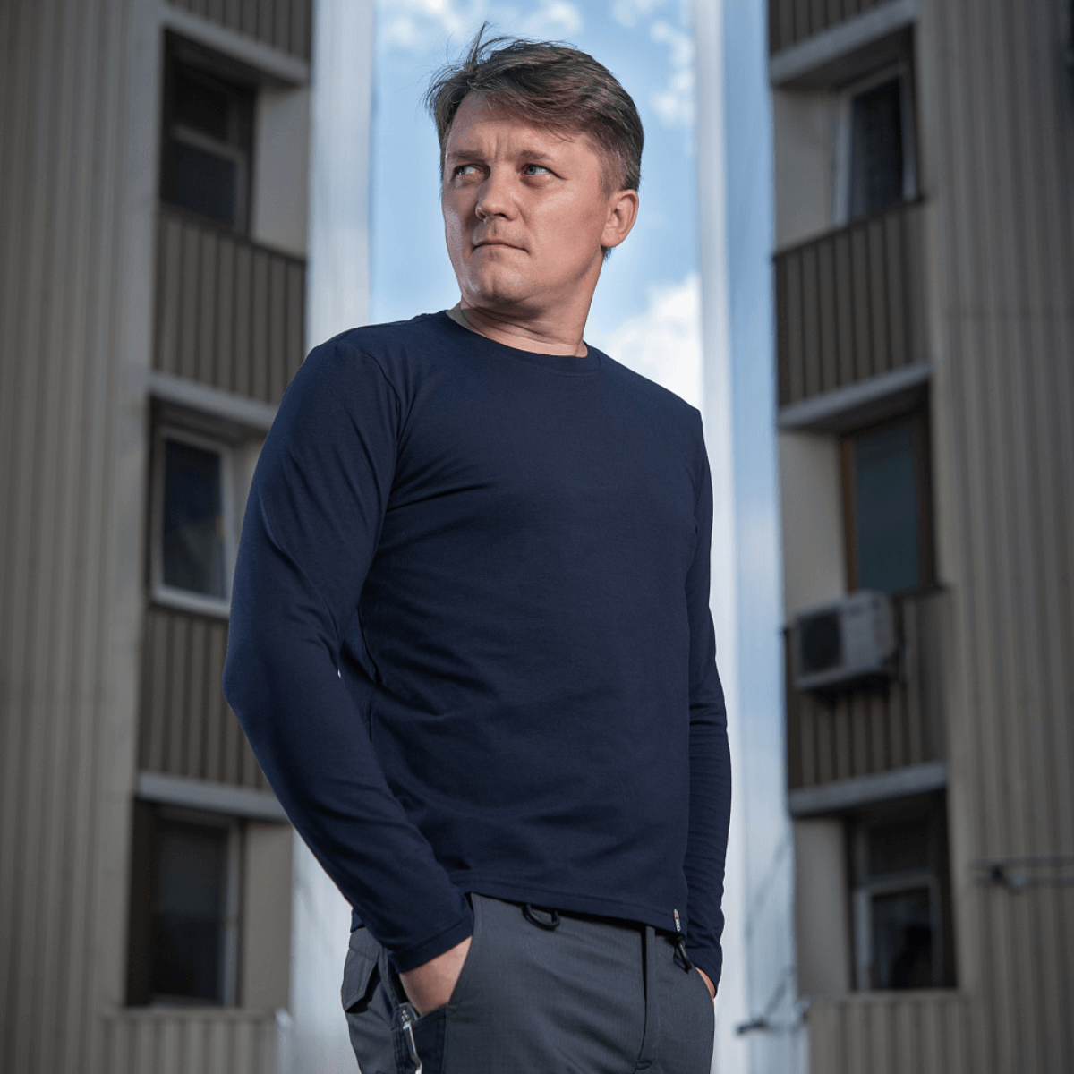 Mies M-Tac Long-sleeve T-shirt 93/7 päällä rakennuksen edessä, 93% puuvillaa ja 7% elastaania kestävyyttä ja muotopysyvyyttä varten.