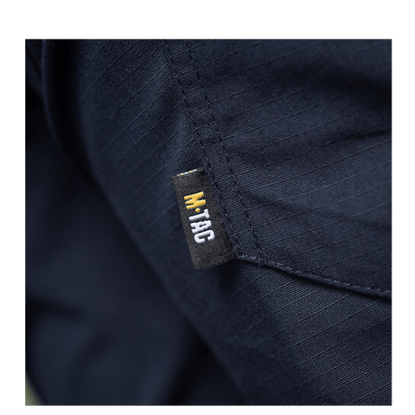 Yksityiskohta M-Tac Bukser Aggressor Dame Flex -housuista, M-Tac-logo tummansinisellä kankaalla.