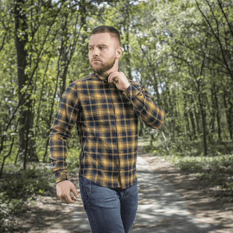 Mies M-Tac Redneck -paidassa navy sininen/keltainen työ- ja vapaa-ajan käyttöön, säädettävät hihat, kävelee metsäalueella.