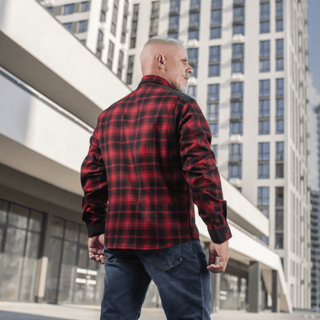 Mies pukeutuneena M-Tac Redneck -paitaan punaruutuisena, modernin rakennuksen edessä, sopii työhön ja vapaa-aikaan mukavalla istuvuudella.