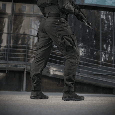 Mies pitää yllä M-Tac STURM NyCo Extreme Gen.II -housuja joustavilla inserteillä, suunniteltu taktiseen käyttöön, kuvattu ulkona.