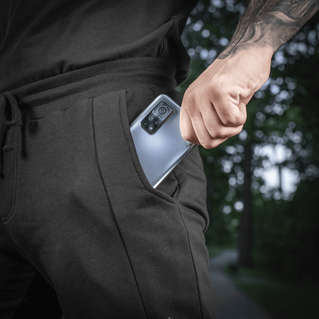 Mies pukeutuneena M-Tac Shorts Casual Fit Cotton -shortseihin, puhelin taskussa, esittelee käytettävyyden ja muotoilun.