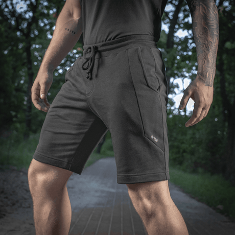 Mies pukeutuneena M-Tac Shorts Casual Fit Cotton -shortseihin, mustat taskuilla ja kuminauhalla vyötäröllä, ihanteelliset aktiiviseen käyttöön, 100% puuvillaa.