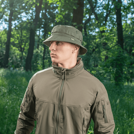 Mies, joka käyttää M-Tac Panama Rip-Stop army-hattua puolijäykkällä lipalla ja ilmanvaihtoaukoilla, seisoo metsässä. Boonie-mallin innoittama.