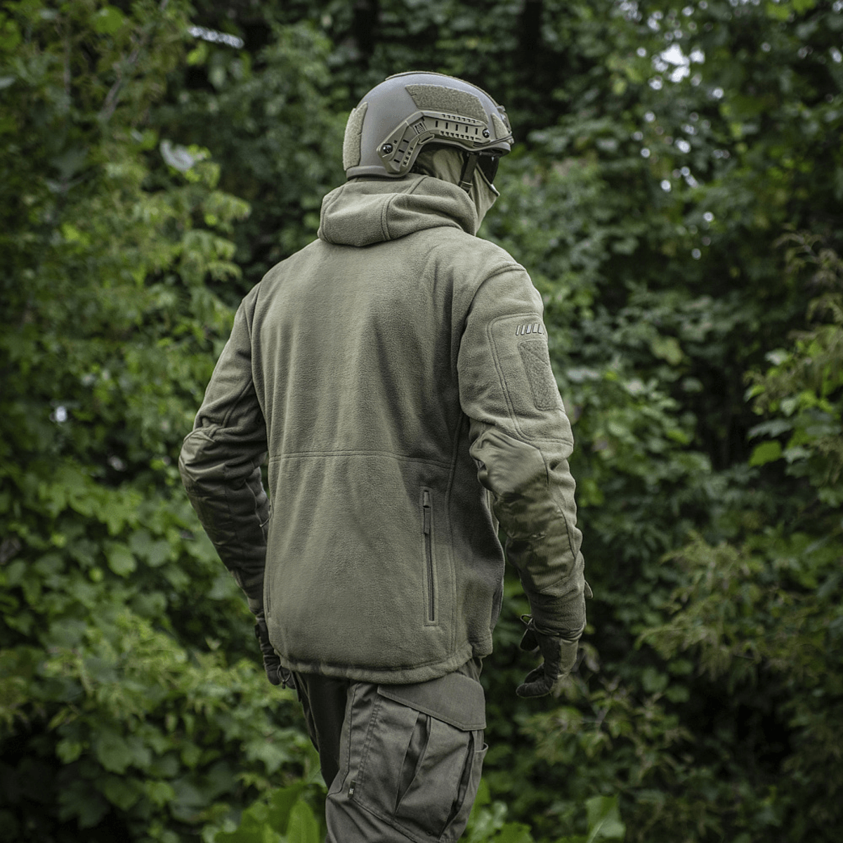 Mies M-Tac Division Gen.II Windblock fleecetakki päällä metsässä, suunniteltu suojaamaan tuulelta ja kylmyydeltä viileässä säässä.