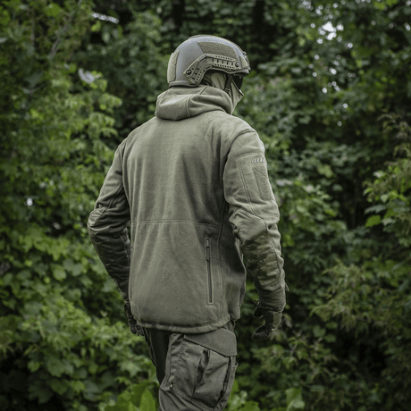 Mies M-Tac Division Gen.II Windblock fleecetakki päällä metsässä, suunniteltu suojaamaan tuulelta ja kylmyydeltä viileässä säässä.