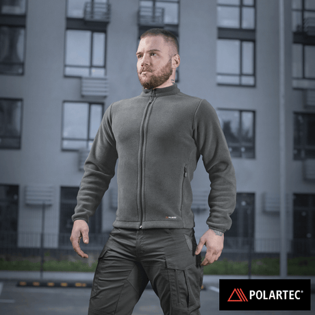 Mies M-Tac Nord Polartec -fleecetakissa, suunniteltu tyyliin ja lämpöön, Polartec® 200 Series -fleecellä asuinrakennuksen taustalla.