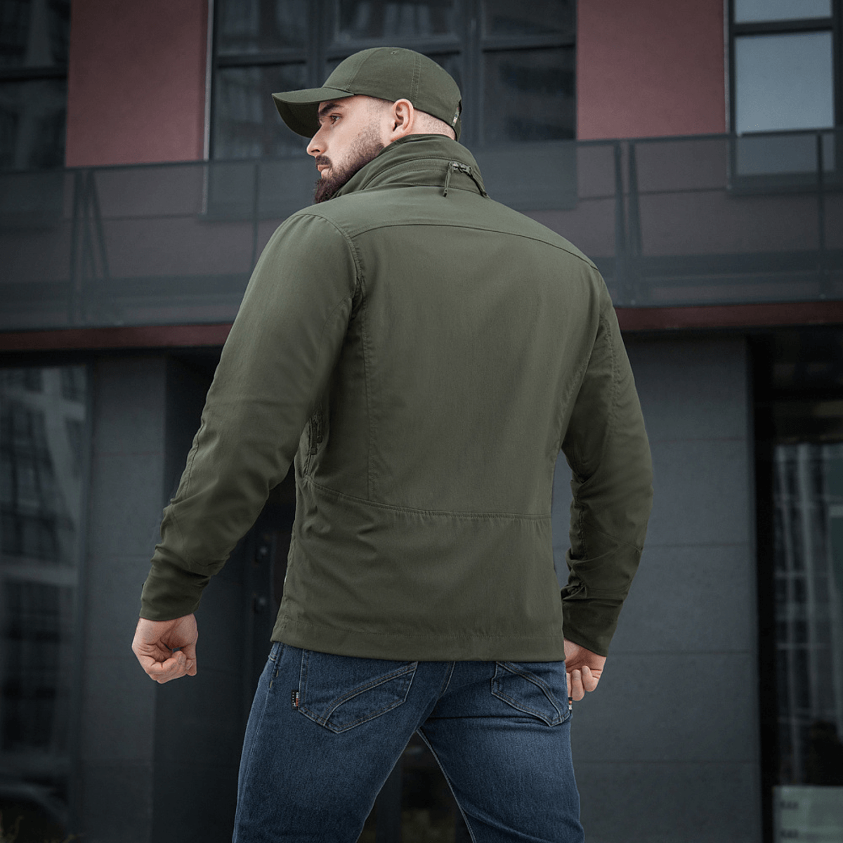 Mies M-Tac Flash -takissa modernin rakennuksen edessä. Kevyt ja monikäyttöinen takki arkeen ja aktiviteetteihin. Ei tarrapaloja hihoissa.