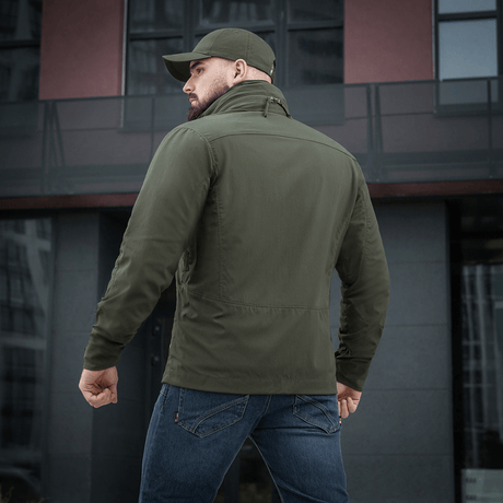 Mies M-Tac Flash -takissa modernin rakennuksen edessä. Kevyt ja monikäyttöinen takki arkeen ja aktiviteetteihin. Ei tarrapaloja hihoissa.