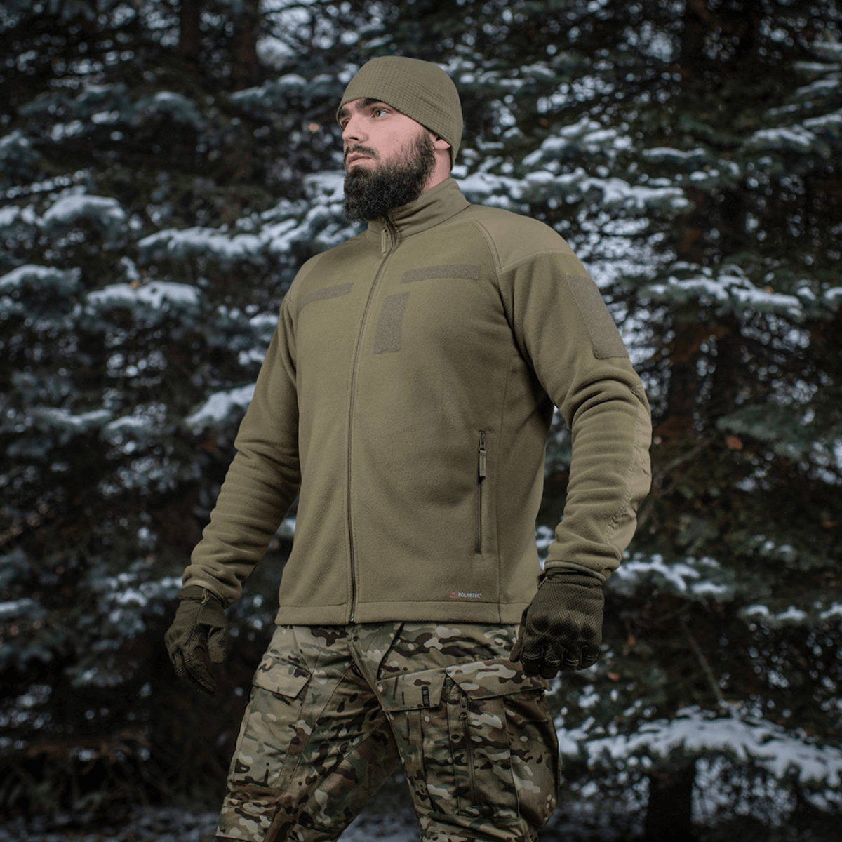 Mies pukeutuneena M-Tac Combat Fleece Polartec -takkiin metsässä, korostaa taktikointiin sopivaa muotoilua.