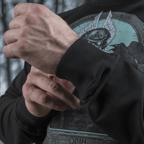 Mies säätää M-Tac Raglan Odin Mystery -paidan hihaa Odin-kuviolla, valmistettu miellyttävästä puuvilla-elastaanikankaasta, sopii arkeen.
